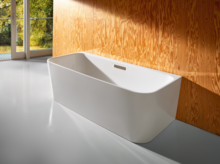 Freestanding rectangular steel enamel bathtub with rounded corners in front of a wood-effect wall.