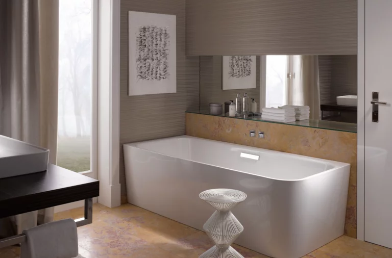 Vasca da bagno rettangolare autoportante in acciaio smaltato, accanto lavabo su piano d’appoggio scuro, bagno moderno.