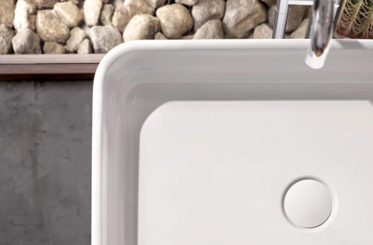 矩形钢搪瓷洗脸盆嵌入式台面，白色表面，现代水龙头，背景有鹅卵石。