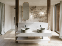 Modernes Badezimmer mit zwei grauen Waschtischen auf weißer Konsole, ovalem Spiegel und großflächiger Natursteinoptik.