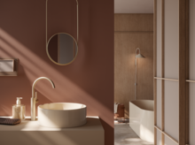 Rundes Stahl-Email-Waschbecken auf Einbauplatte, ovale Stahl-Email-Badewanne im Hintergrund, modernes Bad mit warmen Farbtönen.