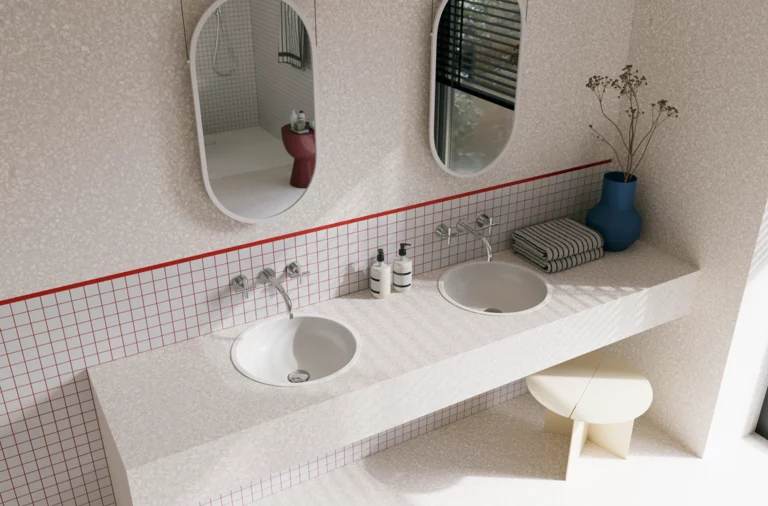 Helles Badezimmer mit zwei weißen Waschtischen, ovalen Spiegeln, gefliester Ablage und roten Akzenten an der Wand.