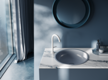 钢瓷圆形洗脸盆安装在台面上，配水龙头、镜子和置物架，现代浴室。