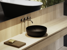 Schwarzer, runder Aufsatzwaschtisch auf heller Holzplatte mit Wandarmatur und Seifenablage im modernen Badezimmer.