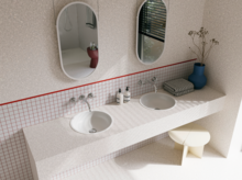 Helles Badezimmer mit zwei weißen Waschtischen, ovalen Spiegeln, gefliester Ablage und roten Akzenten an der Wand.