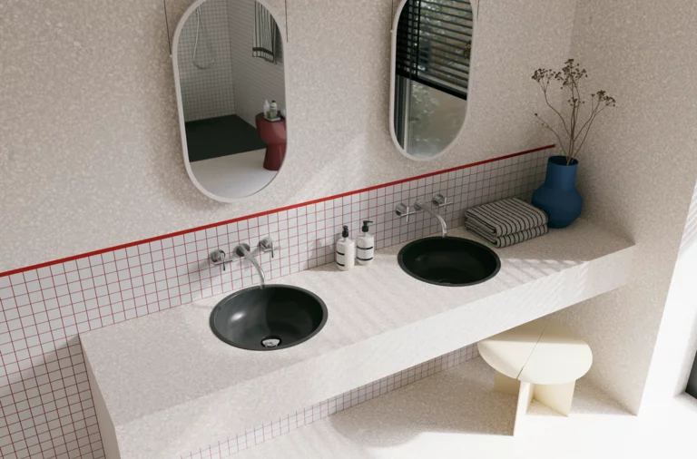 Helles Badezimmer mit zwei dunkelgrauen Waschtischen, ovalen Spiegeln, gefliester Ablage und roter Linie an der Wand.