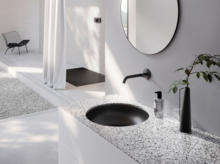 Круглая стальная эмалированная раковина в черной столешнице перед стеной с зеркалом, современный смеситель, декоративные элементы.