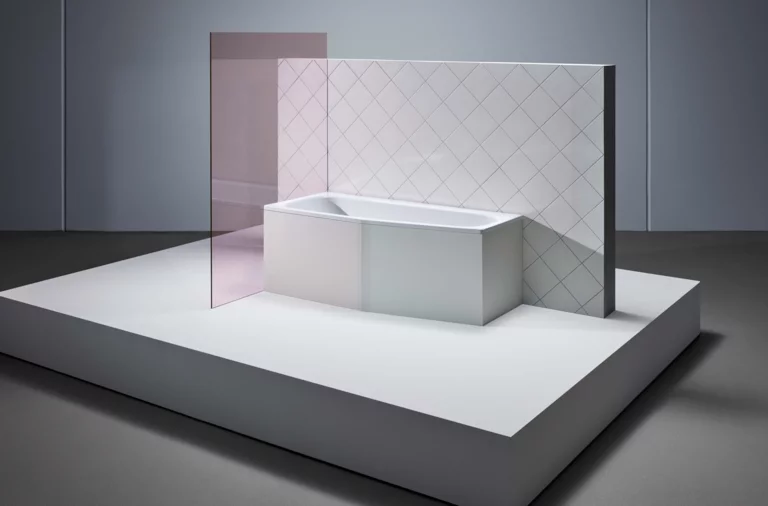 Bañera rectangular de acero esmaltado con esquina biselada, frente a pared alicatada y mampara de ducha de vidrio.