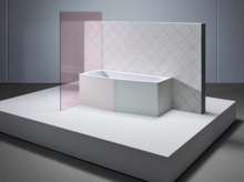 Bañera rectangular de acero esmaltado con esquina biselada, frente a pared alicatada y mampara de ducha de vidrio.