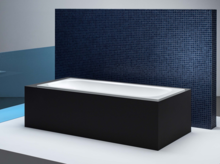 Vasca da bagno rettangolare in acciaio smaltato con bordi dritti, davanti a parete a mosaico blu e separé in vetro.