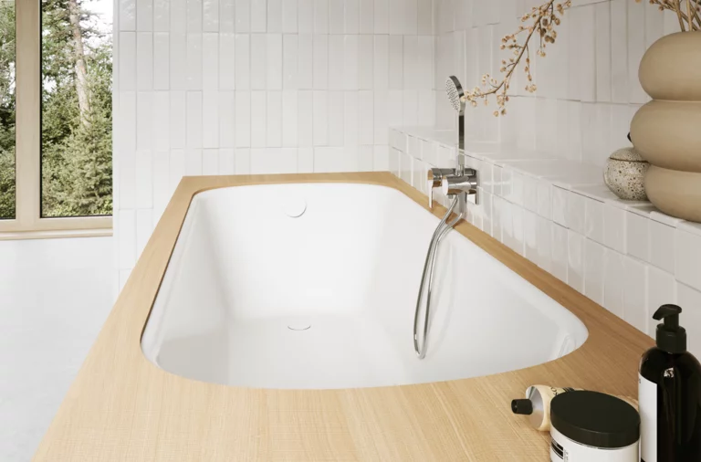 Helles Bad mit eingelassener Badewanne, weißer Innenfläche, beiger Einfassung, Fenster, Armatur und Pflegeprodukten.