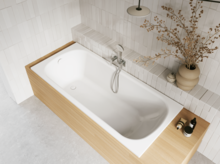 Aufsicht auf helles Bad mit eingelassener weißer Badewanne, beiger Einfassung, Armatur, Vase und Pflegeprodukten.