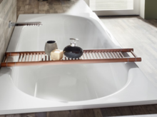 Rectangular steel enamel bathtub, glossy white, with wooden tray and bathroom accessories, in modern bathroom.