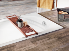 Rectangular steel enamel bathtub, flat built-in, with wooden tray, soap dispenser and soap, on wooden floor.