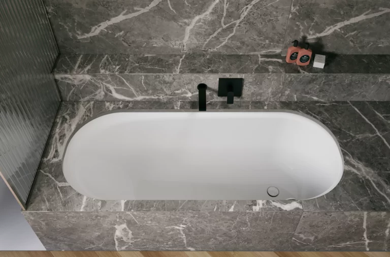 White glazed titanium-steel bathtub set in a grey stone-look surround, with a black wall-mounted faucet.