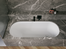 White glazed titanium-steel bathtub set in a grey stone-look surround, with a black wall-mounted faucet.