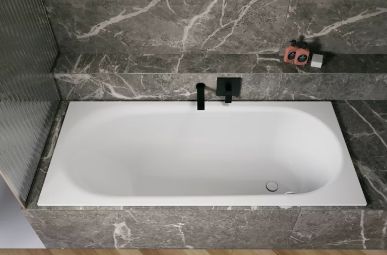 White glazed titanium-steel bathtub in a grey stone-look surround, with a black wall-mounted faucet.