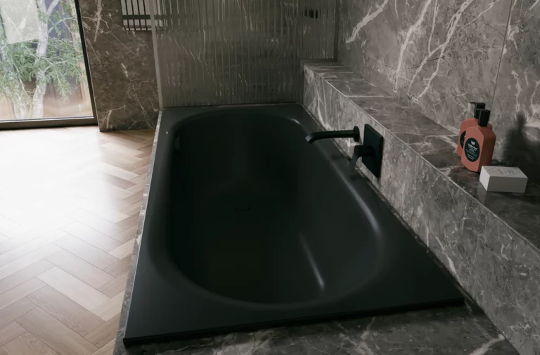 Black glazed titanium-steel bathtub in a grey stone-look setting, with black wall faucet and window.