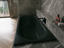 Black glazed titanium-steel bathtub in a grey stone-look setting, with black wall faucet and window.