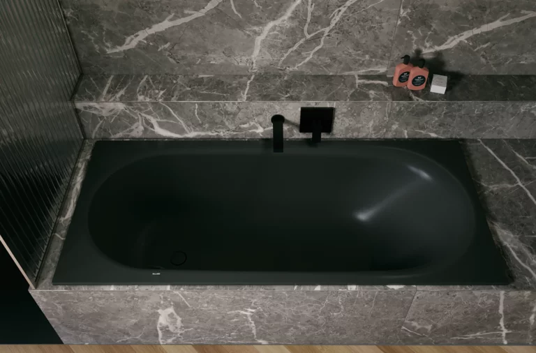 Black glazed titanium-steel bathtub in a grey stone-look surround, with black wall faucet and shelf.