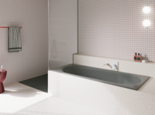 Grey glazed titanium-steel bathtub in a bright bathroom with white tiles, wall faucet and open shower.