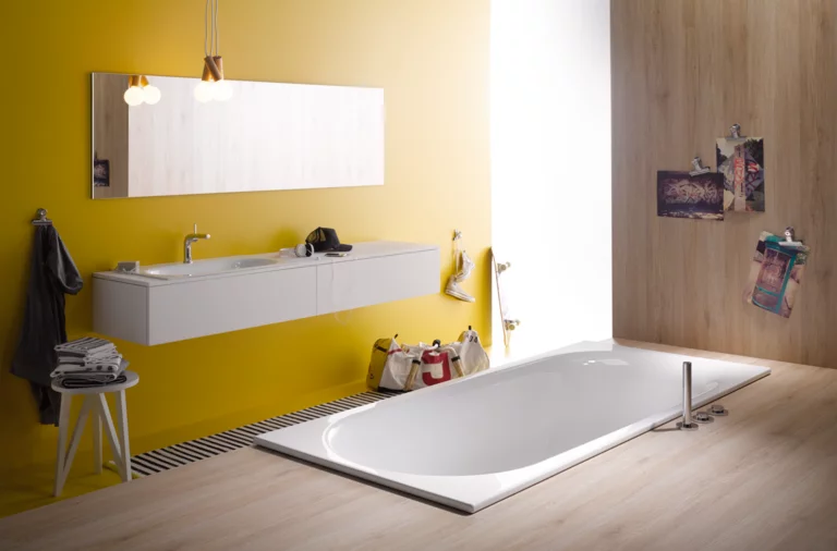 Baignoire rectangulaire en acier émaillé, lavabo sur plan, salle de bains moderne avec mur jaune et aspect bois.
