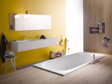Baignoire rectangulaire en acier émaillé, lavabo sur plan, salle de bains moderne avec mur jaune et aspect bois.