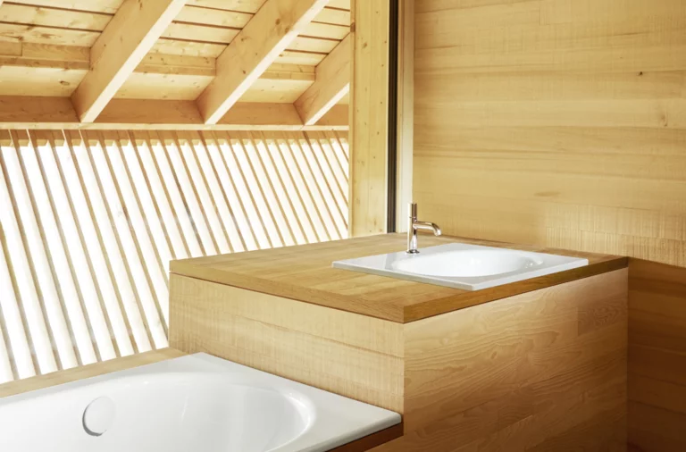 Rechteckige Stahl-Email-Badewanne und quadratisches Stahl-Email-Waschbecken auf Einbauplatte in hellem Holzbad.