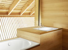 Rechteckige Stahl-Email-Badewanne und quadratisches Stahl-Email-Waschbecken auf Einbauplatte in hellem Holzbad.