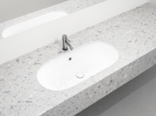 Oval white inset washbasin in terrazzo-style countertop with silver faucet and mirror in the background.