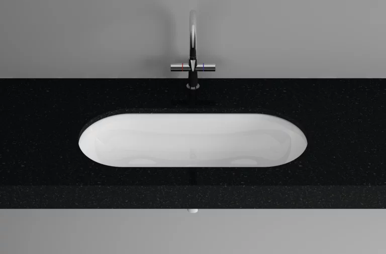 Ovales Stahl-Email Waschbecken in weiß, flächenbündig in schwarze Einbauplatte integriert, moderne Armatur darüber.