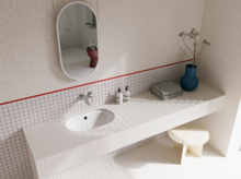 Helles Badezimmer mit weißem Waschtisch, ovalem Spiegel, gefliester Ablage und roter Akzentlinie an der Wand.
