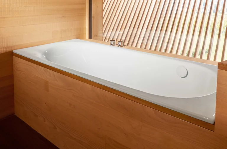 Rechteckige Badewanne aus Stahl-Email, weiß, in eine Holzverkleidung eingebaut, mit Armatur am Rand.