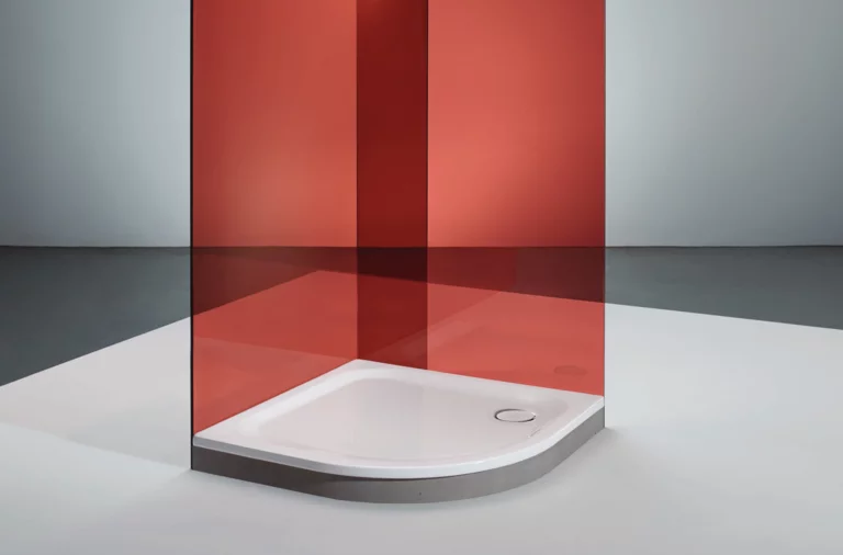 Douchebak van staal-email, kwartrond, gelijkvloers, met rode glazen wand in moderne, minimalistische ruimte.