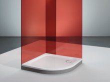 Douchebak van staal-email, kwartrond, gelijkvloers, met rode glazen wand in moderne, minimalistische ruimte.