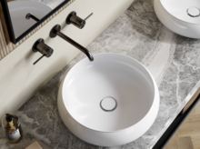 Deux vasques rondes sur plan en marbre gris, robinets muraux, miroirs et sol en bois clair.