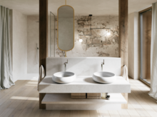 Modernes Badezimmer mit zwei weißen Waschtischen auf breiter Konsole, ovalem Spiegel und markanter Wand in Natursteinoptik.