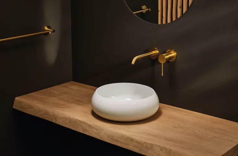 Lavabo rond blanc sur plan en bois, robinet mural et miroir rond dans salle de bain moderne.