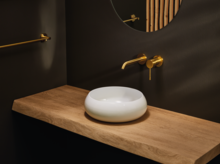 Lavabo rond blanc sur plan en bois, robinet mural et miroir rond dans salle de bain moderne.