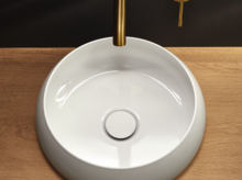 Lavabo rond en acier émaillé sur plan de travail en bois, robinet mural et levier de commande aspect or.