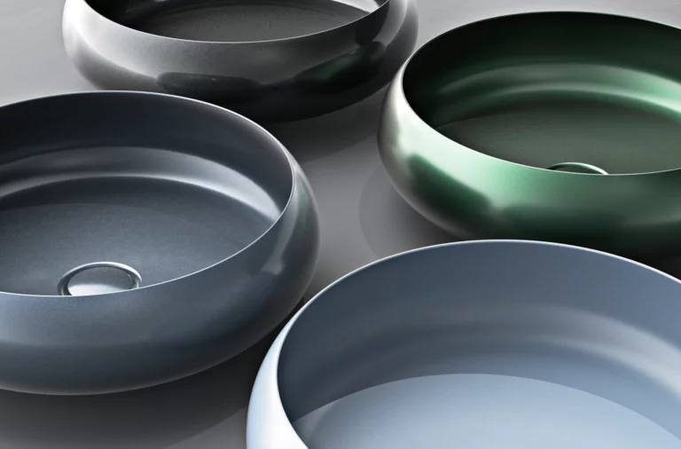 Quatre lavabos ronds en acier émaillé de différentes couleurs, disposés sur un plan de travail.