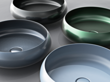 Quatre lavabos ronds en acier émaillé de différentes couleurs, disposés sur un plan de travail.