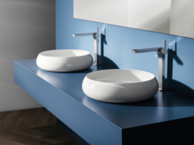 Zwei runde, weiße Waschbecken auf blauer Einbauplatte, jeweils mit modernem Wasserhahn, vor blauer Wand.