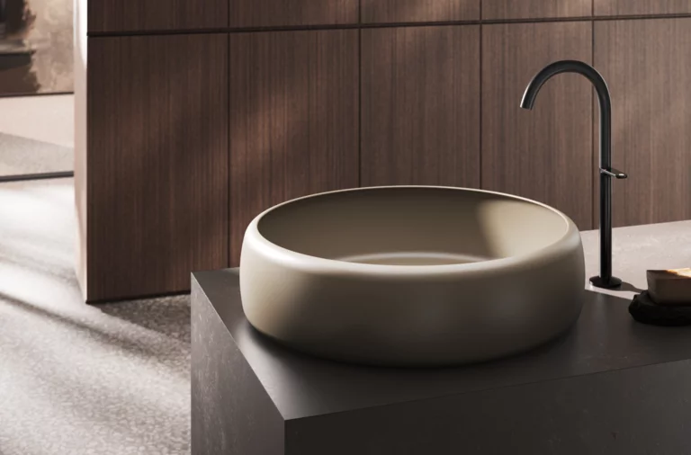 Ronde, diepe wastafel op donker blad met hoge kraan in moderne badkamer.