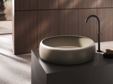 Ronde, diepe wastafel op donker blad met hoge kraan in moderne badkamer.