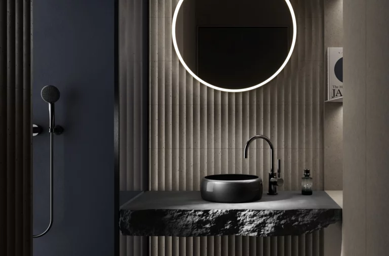 Ronde wastafel op donker blad, erboven ronde spiegel met verlichting, rechts fles, links wanddouche.