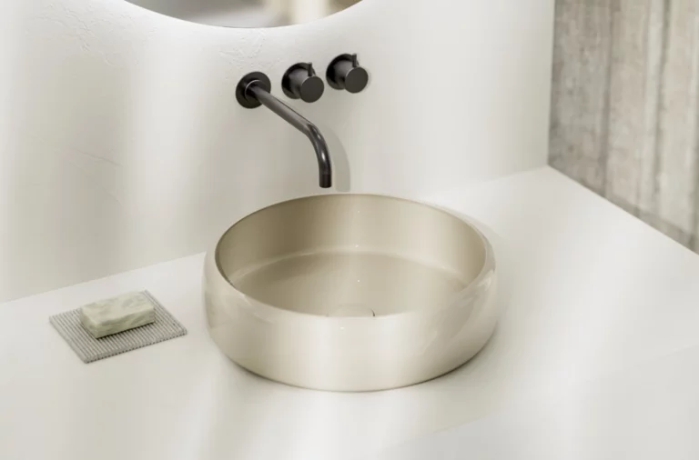 Modernes, rundes Aufsatzwaschbecken in hellem Beige auf weißer Konsole mit schwarzer Wandarmatur und Seifenablage.