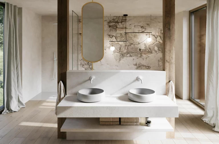 Modernes Badezimmer mit zwei hellgrauen Waschtischen auf breiter Konsole, ovalem Spiegel und markanter Wand in Natursteinoptik.