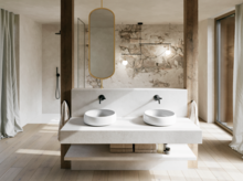 Modernes Badezimmer mit zwei weißen Waschtischen, schwarzen Wandarmaturen, ovalem Spiegel und markanter Wand in Natursteinoptik.
