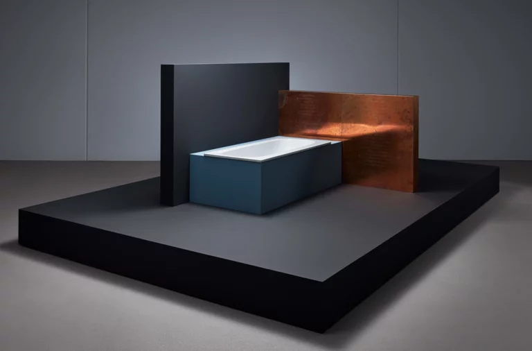 Rechteckige Badewanne aus Stahl-Email in moderner Umgebung, seitlich von dunklen und kupferfarbenen Wänden umgeben.